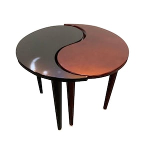 May include: A set of two nesting tables shaped like a yin yang symbol. The top table is dark brown and the bottom table is a lighter shade of brown.