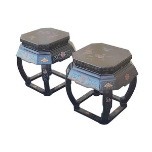 May include: Two black octagonal wooden stools with intricate floral and butterfly designs painted in gold, blue, and pink. The stools have a square base and curved legs.