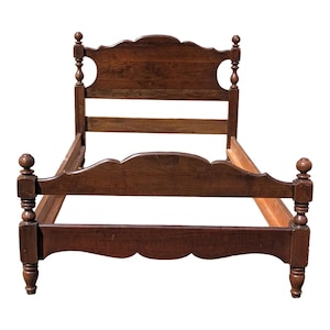 May include: A dark brown wooden bed frame with a headboard and footboard. The headboard has a curved top with decorative cutouts. The frame features turned posts and a scalloped design along the bottom. The bed frame is made of wood.