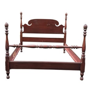 May include: A dark brown, four-poster bed frame with a headboard and footboard. The bed frame has decorative finials on the posts and a detailed design on the headboard. The bed frame is made of wood and is empty.