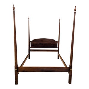 May include: A dark brown four-poster bed frame. The bed frame has a headboard and footboard, with four tall posts at each corner. The posts are topped with decorative finials. The bed frame is made of wood.