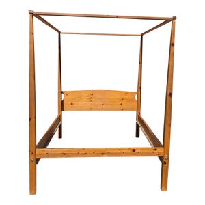 May include: A wooden canopy bed frame with a natural finish. The bed frame has four tall posts connected by horizontal beams, creating a rectangular canopy. The headboard is a solid piece of wood with a curved top.