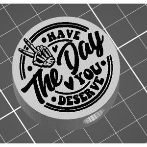 May include: A round, gray, rubber stamp with black ink. The stamp reads "Have the Day You Deserve" with a peace sign and heart design.