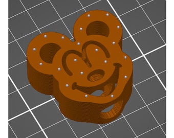 May include: A brown 3D printed Mickey Mouse head with a smiling face and large ears. The head is decorated with small silver dots.