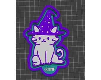 May include: A white cat wearing a purple and blue witch hat with stars. The cat is sitting with its tail curled around its legs. The image is a 3D model of a cookie cutter.