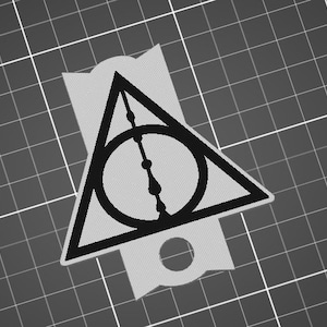 Puede incluir: Pegatina en blanco y negro con el símbolo de las Reliquias de la Muerte de la serie Harry Potter. El símbolo es un triángulo con un círculo en su interior y una línea vertical que lo atraviesa.