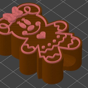 May include: A brown gingerbread person cookie cutter with pink details. The cookie cutter is shaped like a person with a bow on its head, a heart on its chest, and a skirt.