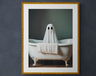 May include: A framed photograph of a white ghost in a bathtub. The ghost is wearing a white sheet and has two black eyes. The bathtub is white with gold feet and is sitting on a wooden floor. The frame is gold.