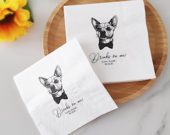May include: White paper napkins with a black and white illustration of a dog wearing a bow tie. The napkins have the text "Drinks on me! Love, Louie 09.14.23" in a script font. The napkins are on a wooden tray.