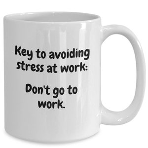 May include: White ceramic mug with a curved handle. The mug features black text that reads, "Key to avoiding stress at work: Don't go to work."