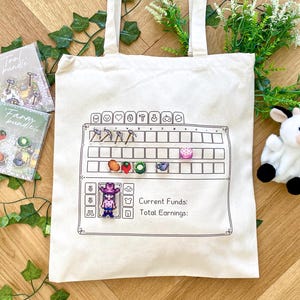 May include: A white canvas tote bag with a black and white design of a video game-style farm. The design includes a grid with icons for tools, crops, and a character. The text "Current Funds: Total Earnings:" is also included in the design. The bag is surrounded by green plants and a white stuffed cow.