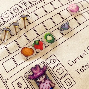 May include: A white canvas tote bag with a brown outline of a video game interface. The interface has a grid of squares with various pixelated icons, including a pickaxe, a watering can, a pumpkin, a heart, and a shirt. The text "Current" and "Total" are visible on the interface. A pixelated character wearing a pink hat and a pink shirt is on the bag.