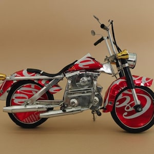 May include: A handcrafted motorcycle sculpture made from recycled materials. The bike features a red and white design, with silver accents, black tires, and gold-colored details on the headlights and exhaust pipes. The motorcycle is a decorative item.