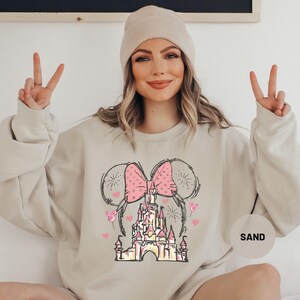a woman sitting on a bed wearing a mickey mouse sweatshirt