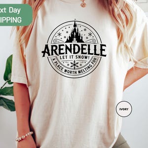 A person wearing a white t-shirt with a graphic design featuring a castle and snowflakes.