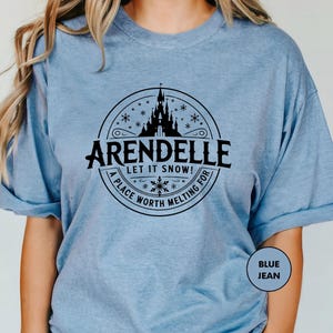 A woman wearing a light blue t-shirt with a graphic design featuring a castle and snowflakes.
