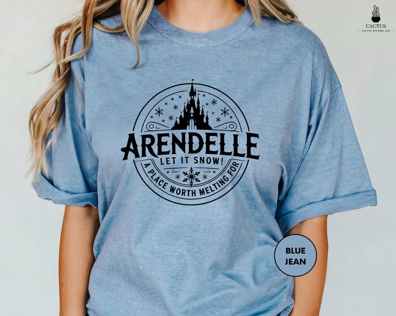 A woman wearing a light blue t-shirt with a graphic design featuring a castle and snowflakes.