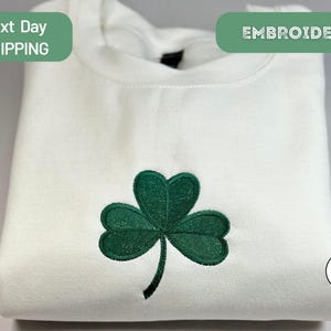 a white t - shirt with a green clover embroidered on it