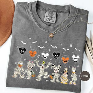 A gray t-shirt with a Halloween-themed design featuring various Disney characters such as Mickey Mouse, Minnie Mouse, Donald Duck, Goofy, and Pluto, along with bats, stars, and a pumpkin.