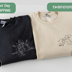 May include: Two sweatshirts with embroidered designs. The black sweatshirt has a design of five hands forming a fist with the word "DAD" and the names "Alex, Harley, John, Kate, Josh" embroidered on the hands. The sand colored sweatshirt has a design of two hands forming a fist with the word "DAD" and the name "Amy" embroidered on the hands.