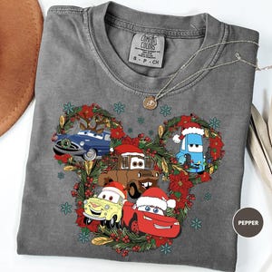 A gray t-shirt with a Christmas-themed design featuring cartoon cars and decorations, including a wreath and snowflakes.
