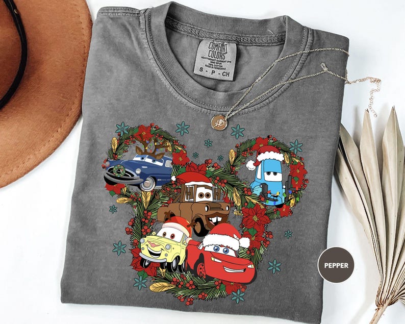 A gray t-shirt with a Christmas-themed design featuring cartoon cars and decorations, including a wreath and snowflakes.