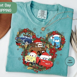 A turquoise t-shirt with a Christmas-themed design featuring cartoon cars and wreaths.
