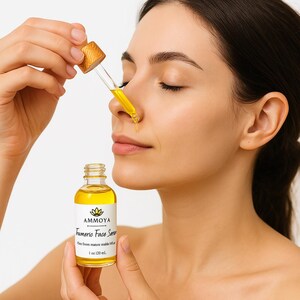 K&ouml;nnte beinhalten: Eine durchsichtige Glasflasche mit einer gelben Fl&uuml;ssigkeit. Die Flasche hat ein wei&szlig;es Etikett mit dem Text "AMMOYA Turmeric Face Serum" und "1 oz (30 ml)". Eine Person h&auml;lt die Flasche und tr&auml;gt das Serum auf ihr Gesicht auf.