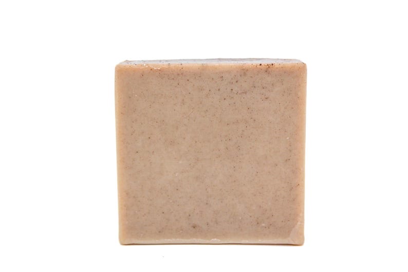 May include: A square bar of soap with a light brown color and a grainy texture.