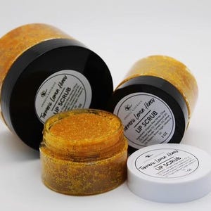 Könnte beinhalten: Drei Gläser mit Kurkuma-Zitronen-Honig-Lippenpeeling. Die Gläser sind mit einem leuchtend gelben Peeling gefüllt und haben schwarze Deckel. Die Etiketten auf den Gläsern lauten "Kurkuma-Zitronen-Honig-Lippenpeeling".