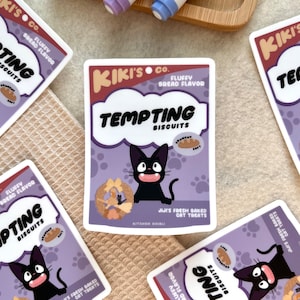 May include: A sticker featuring a cartoon black cat with a white cloud behind it. The sticker is a parody of a cat food box and reads "Kiki's Co. Fluffy Bread Flavour Tempting Biscuits" with a small image of a bread loaf and the text "Jiji's Fresh Baked Cat Treats Kitchen Ghibli".