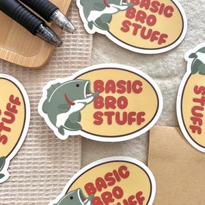 May include: Four white oval stickers with a yellow background and a cartoon bass fish. The text on the stickers reads "Basic Bro Stuff".