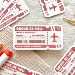 May include: A pink and white sticker with the text "Broke as Hell" and a plane ticket design. The sticker says "Now Boarding" and has the words "Origin: Reality" and "Destination: La La Land".