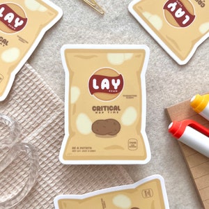 May include: A brown and white Lay's potato chip bag sticker with the text "Lay's Down" and "Critical Nap Time". The bag has a brown potato inside and the text "Be a Potato, Net Wt. Just a Snov" at the bottom.