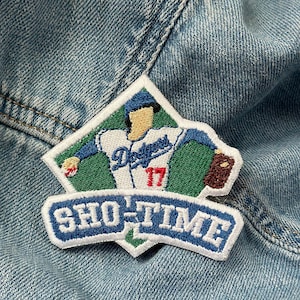 以下が含まれることがあります： ロサンゼルス・ドジャースのユニフォームを着た野球選手が描かれた刺繍パッチ。ユニフォームには背番号17が記されている。パッチは青、緑、白で、青い背景に白い文字で「SHOW-TIME」と書かれている。