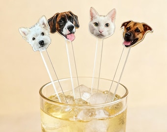 Könnte beinhalten: Ein Glas mit gelber Flüssigkeit und Eiswürfeln, in dem sich vier Cocktail-Rührstäbchen befinden. Jedes Rührstäbchen zeigt ein anderes Tiergesicht: eine weiße Katze und Hunde. Die Rührstäbchen sind im Getränk platziert.