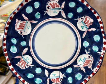 May include: A hand-painted ceramic plate with a navy blue background, featuring white and red fish designs. The plate has a white center, a scalloped edge, and is decorated with teal bubbles and red dots.