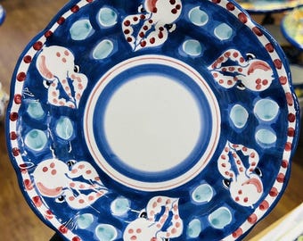May include: A blue ceramic plate with a scalloped edge, featuring a white center and a blue and white striped border. The plate is decorated with octopus designs in white and red, and blue and white dots.