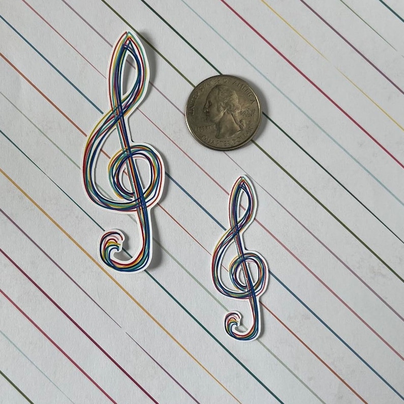 May include: Two treble clef stickers with a rainbow-colored outline. The stickers are on a white background with diagonal stripes in various colors. A quarter coin is next to the stickers.