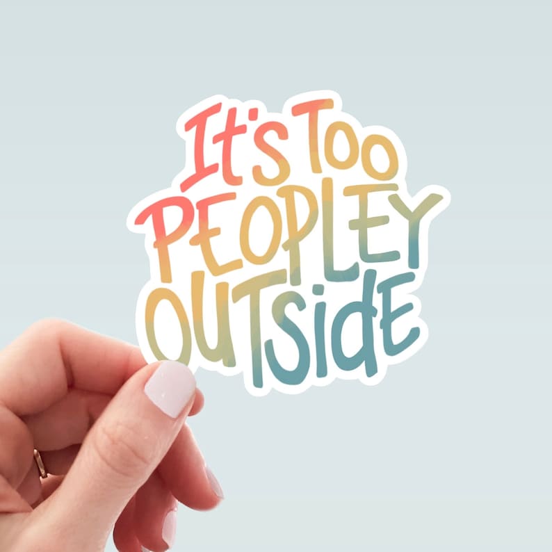 May include: A white sticker featuring the text "It's Too PEOPLEY OUTSIDE" in a colourful, handwritten style. The words change from red to yellow to blue. The sticker is held by a hand against a pale blue backdrop.