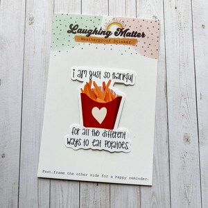 May include: A white sticker with a red and white illustration of a container of french fries. The text on the sticker reads "I am just so thankful for all the different ways to eat potatoes."  The sticker also has the text "Laughing Matter Weatherproof Sticker" at the top.