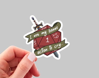 May include: A red 20-sided die with a sword through it and a green banner that reads "I use my bonus action to cry..." The die shows a 1.