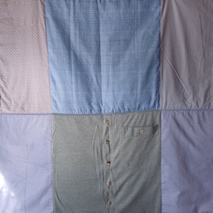 Könnte beinhalten: Eine Patchwork-Decke aus verschiedenen farbigen Hemden. Die Decke besteht aus vier Quadraten, jedes mit einem anderen Muster. Das obere linke Quadrat ist helllila mit einem kleinen weißen Muster. Das obere rechte Quadrat ist hellblau mit einem weißen Karomuster. Das untere linke Quadrat ist hellblau mit einer einfarbigen Farbe. Das untere rechte Quadrat ist hellblau mit einer einfarbigen Farbe.
