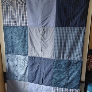 Könnte beinhalten: Eine Patchwork-Decke aus verschiedenen blauen Hemden mit einer Mischung aus Mustern wie Karos, Vichy, Streifen und einem Palmenblatt-Druck. Das Design enthält sichtbare Hemdknöpfe, Kragen und Taschen, die über die Stoffquadrate verteilt sind.