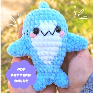 May include: A handmade, light blue crocheted shark plushie with white belly and accents. The shark has black eyes, pink cheeks, and a white zig-zag mouth. Text on the image reads "PDF PATTERN ONLY!!".