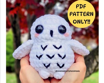 Op de afbeelding: Een wit gebreid knuffeldier in de vorm van een uil met zwarte ogen en een zwart-wit patroon op zijn borst. De uil wordt vastgehouden door een hand. De tekst "PDF PATTERN ONLY!!" staat in een gele cirkel boven de uil. De tekst "@lovemedeerlyhandmade" staat onder de uil.