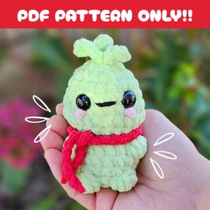 May include: A crocheted green plushie with a red scarf, black eyes, and pink cheeks. The plushie has a sprout-like top and is held in a hand. Text at the top reads "PDF PATTERN ONLY!!".