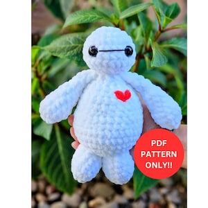 Puede incluir: Una muñeca blanca de ganchillo hecha a mano con un corazón rojo en el pecho. La muñeca tiene ojos negros y una línea negra encima. La imagen incluye un círculo rojo con el texto "PDF PATTERN ONLY!!".
