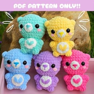 Może przedstawiać: Pięć pluszowych misiów wykonanych na szydełku w różnych kolorach: jasnoniebieski, żółty, fioletowy, różowy i jasnoniebieski. Każdy miś ma sercowaty wzór na klatce piersiowej i czarne oczy.