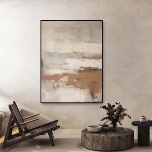 May include: Abstract painting in shades of brown, white, and gray. The painting is framed in a black frame and hangs on a light beige wall.